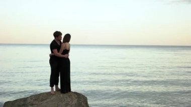 Denizin kenarında kayanın üzerine siyah giyim kucaklayan içinde çift