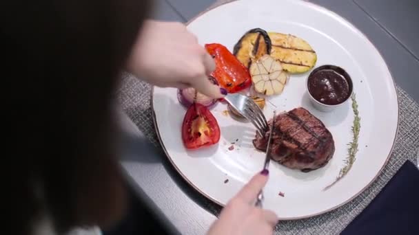 Женщина режет стейк на тарелке — стоковое видео