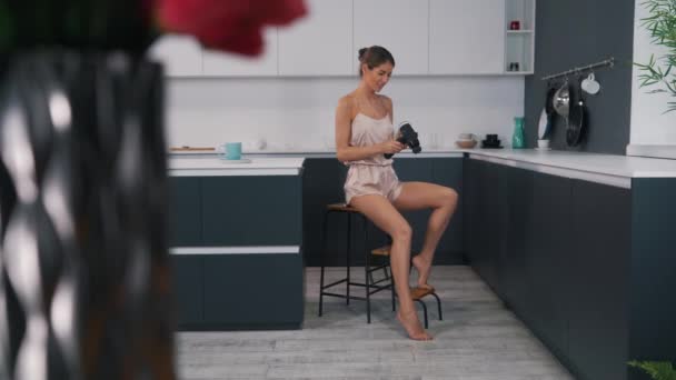 Ragazza utilizza un massaggiatore corpo mentre seduto in cucina — Video Stock