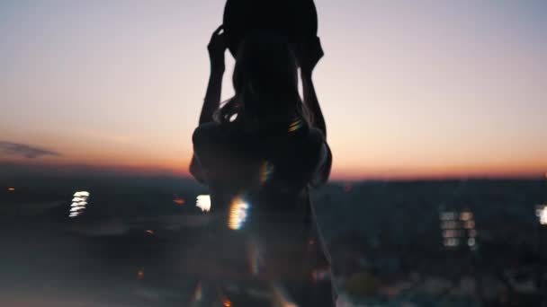 Lány felvesz egy kalapot naplementekor a háttérben a város — Stock videók