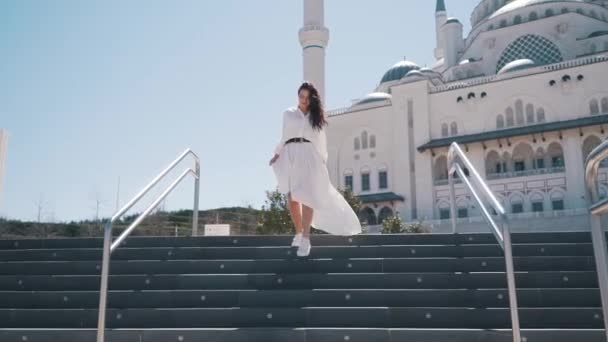 하얀 드레스를 입은 소녀가 흰 모스크 옆을 걷고 있습니다. — 비디오