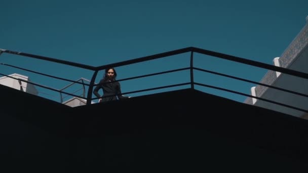 Дівчина в суворому чорному одязі на фоні архітектури — стокове відео
