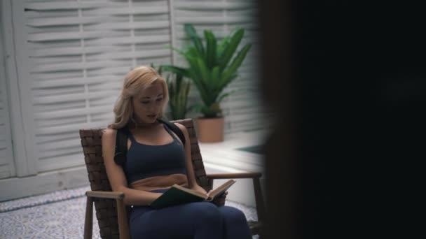 Menina em um espartilho de esportes lendo um livro no quintal — Vídeo de Stock