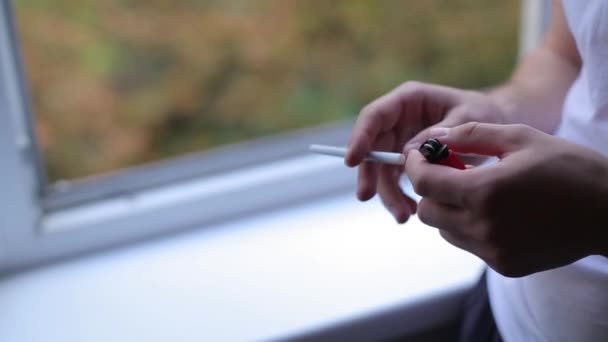 Man tänder en cigarett vid fönstret — Stockvideo