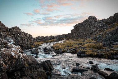Bulutlu gökyüzünün altındaki kayalık arazide nehir akan manzaralı bir yer.
