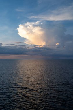 Gün batımında renkli gökyüzünü yansıtan sakin okyanus sularının manzarası.
