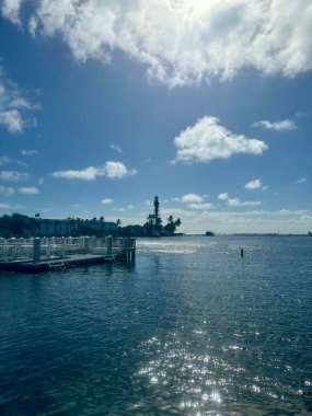 Sakin mavi su, uzak deniz feneri ve parlak gökyüzünün yer aldığı güzel bir rıhtım manzarası..