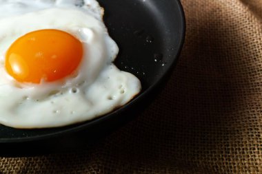 Kahverengi desenli yüzeyde siyah tavada pişmiş yumurta.