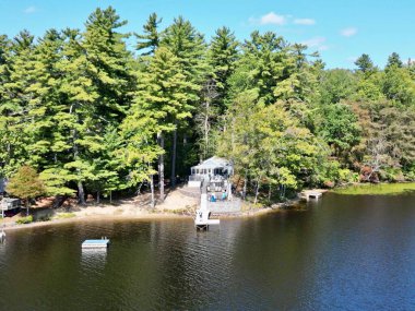 Göl kenarındaki yeşil ağaçlarla çevrili bir kulübenin havadan görüntüsü.