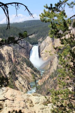 Yeşil ve ağaçlarla çevrili kayalık uçurumlardan şelale düşüyor.