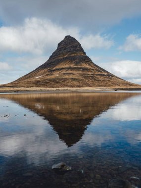 Sakin gölün üzerinde yükselen dağ zirvesi bulutlu gökyüzünü yansıtıyor