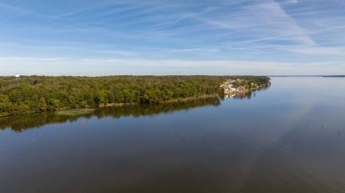 Ağaçları yansıtan sakin suyun ve nehir kıyısındaki mavi gökyüzünün havadan görünüşü.
