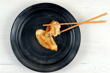 İki parça hamur köftesi siyah yuvarlak tabakta, ahşap çubuklarla duruyor.