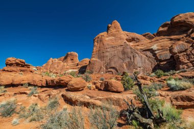 Mavi gökyüzünün altındaki çöl arazisindeki kaya oluşumları.