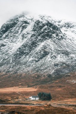 Karla kaplı dağ, küçük beyaz bir ev ve çimenli bir arazi üzerine çöker.