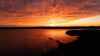 Sakin suyun üzerinde canlı günbatımı renkli bulutları ve ışığı yansıtıyor.