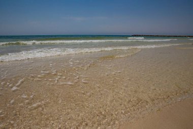 Dalgalar açık mavi gökyüzünün altında temiz kumlu sahili nazikçe yıkıyor..
