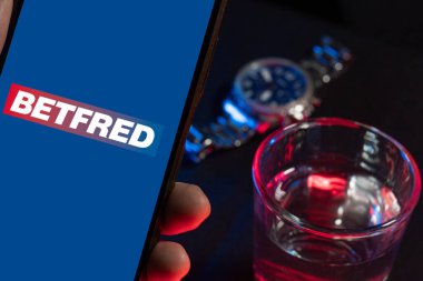 Bogota, Kolombiya - 25 Kasım 2025: Betfred logosu bir elinde karanlık masada, spor bahisleri ve spor ticareti kavramı