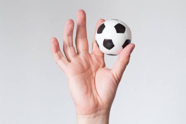 Futbol topu düz arkaplan önünde bir elin başparmağı ve işaret parmağı arasında dengelenmiş. Konsantrasyon, kontrol ve refah için metafor