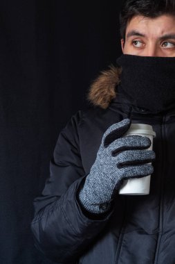Sıcak giysili bir adam yemek kabında sıcak bir içecek tutuyor. Aşırı soğuk ve kentsel kış havasına karşı koruma kavramı.