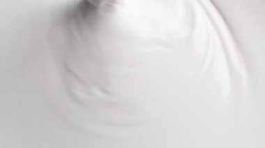 Beyaz boyanın bir kovanın içinde dairesel bir hareketle karıştırıldığı soyut bir video.