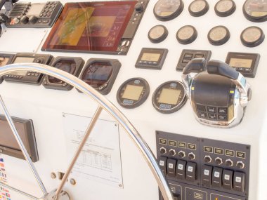 Modern bir tekne dümeninin detaylı bir görüntüsü, büyük paslanmaz çelik bir tekerlek, bir sürü gösterge, bir VHF radyo, navigasyon ekranları