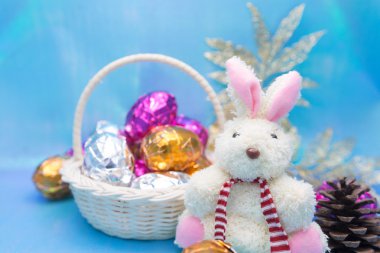 Parlak mavi arka planda renkli yumurtaları olan şirin bir Paskalya tavşanı.