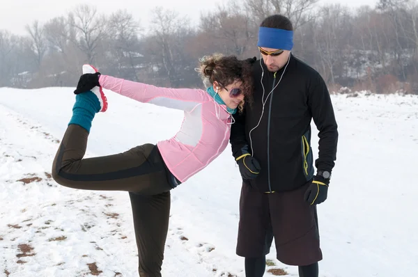 Homem e mulher aquecendo antes de correr para fora na neve — Fotografia de Stock