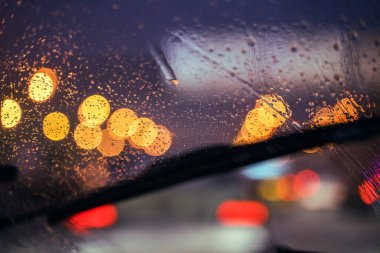 Şehir yolunda Bokeh arka planı. Arabanın ön camında su var. Şehir ışıkları Bokeh. Arabanın camından şehrin gece yolunun görüntüsü geliyor. Gece ışıklarının bulanıklığı Sokakta bokeh