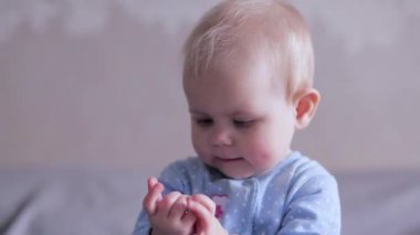 Bir bebek bir yatakta oturuyor ve kendi eli ile oynar