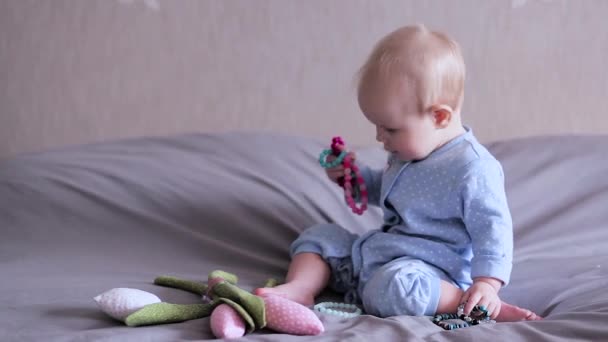 Um bebê em uma cama sentado e brincando com brecelets — Vídeo de Stock