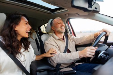 Excited woman laughing and joking with her happy husband while driving to vacation spot, spouses talking and enjoying road trip