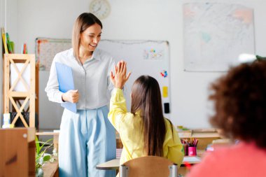 Professional friendly female teacher giving high five to schoolgirl, after successful exam. Education, childhood, teaching, learning and school concept