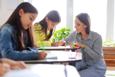 Friendly female teacher helping pupil during test, providing assistance to schoolgirl, fostering an environment of support and focused learning