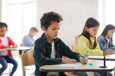 Group of school children studying in classroom, sitting at desks and writing in copybooks during lesson. Education, school and learning concept