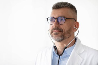 Steteskop takan orta yaşlı bir erkek doktorun portresi beyaz arka planda poz veren gözlüklü bir pratisyen hekim.