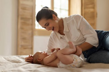 Küçük bebeğiyle oynayıp sohbet eden mutlu bir anne, yatağa uzanan bir anne çocuğuyla vakit geçirmekten zevk alan bir anne, boş bir alan.