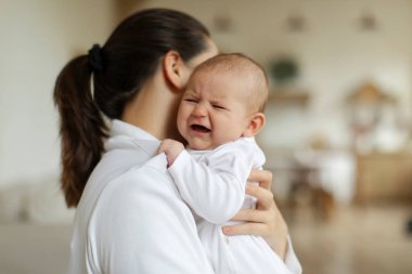 Anne kucağında ağlayan bir kız ya da erkek bebek ve sakinleştirici, dinlendirici bir çocuk yatak odasının içinde, boş yer. Büyüme ve diş çıkarma kavramı