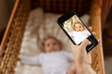 Anne güzel bebeğini akıllı telefondan vuruyor, çocuk beşikte yatıyor, anne çocuğunun ilk yılını yakalıyor.