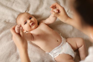 Bakıcı anne her gün egzersiz yapıyor ve bebeğine masaj yapıyor. Yatakta yatıyor ve gülümsüyor.