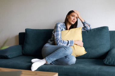 Hüsrana uğramış genç bayan kanepede oturuyor, yastığa sarılıyor, pencereye bakıyor, yanlış karardan pişmanlık duyan mutsuz kadın düşüncelerinde kayboluyor.