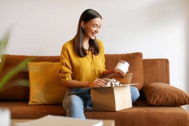 Güzellik kutusu konsepti. Mutlu bayan teslimat paketini aldı, içinde kozmetik ürünleri olan karton paketleri açtı, evdeki koltukta oturdu.
