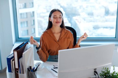 Olumlu iş kadını modern ofiste farkındalık meditasyonu yapıyor, masaüstü bilgisayarının önünde meditasyon yapıyor, iş yerinde sakinliği ve odaklanmayı teşvik ediyor