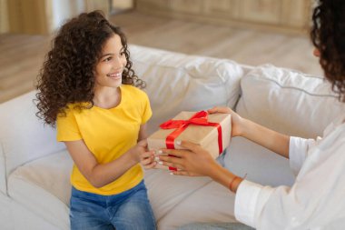 Kız için doğum günü hediyesi. Anneyi sevmek, kızını karşılamak, ona hediye paketi vermek, birlikte bayramı kutlamak, kanepede oturmak.