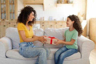 Güzel Latin bir kadın küçük kızına doğum günü hediyesi veriyor, evdeki kanepede oturuyor. Tatil kutlaması konsepti