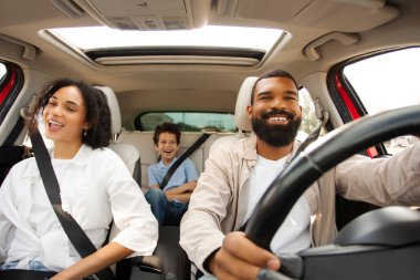 Neşeli siyah aile araba sürerken şarkı söylüyor ve yol boyunca eğleniyor, ebeveynler ve oğullar otomobille seyahat ediyor, ön cam manzaralı