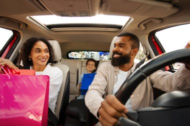 Üç çocuklu mutlu Latin aile, anne-baba ve oğul, renkli alışveriş torbaları taşıyan, araçta oturan ve başarılı alışverişin ardından gülümseyen.