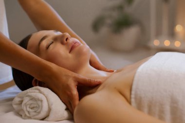 Rahatlamış bir kadın omuz masajı yaptırıyor, lüks bir spa salonuna gidiyor, gözleri kapalı uzanıyor, terapist omuzlarını ovuştururken dinleniyor.