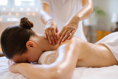 Yetenekli terapistten derin doku masajı alan bir kadın masaj masasında yüzüstü yatan bir kadın, sakin bir atmosfer.