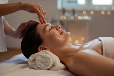 Modern Spa 'da kafa ve yüz masajı yaptıran rahat bir kadının profil fotoğrafı. Terapist masaj yapıyor, alnına masaj yapıyor ve baskı yapıyor.